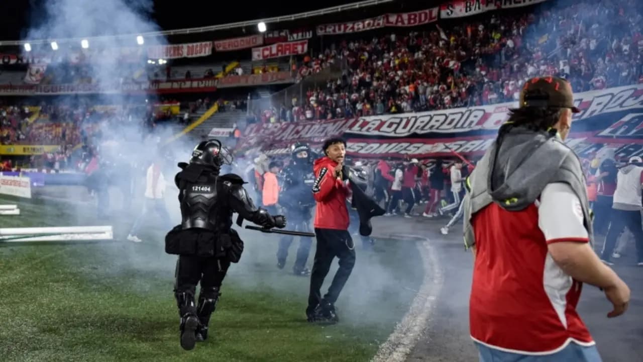 Un policía antidisturbios corre por el césped de El Campín entre gases y aficionados que invadieron la cancha