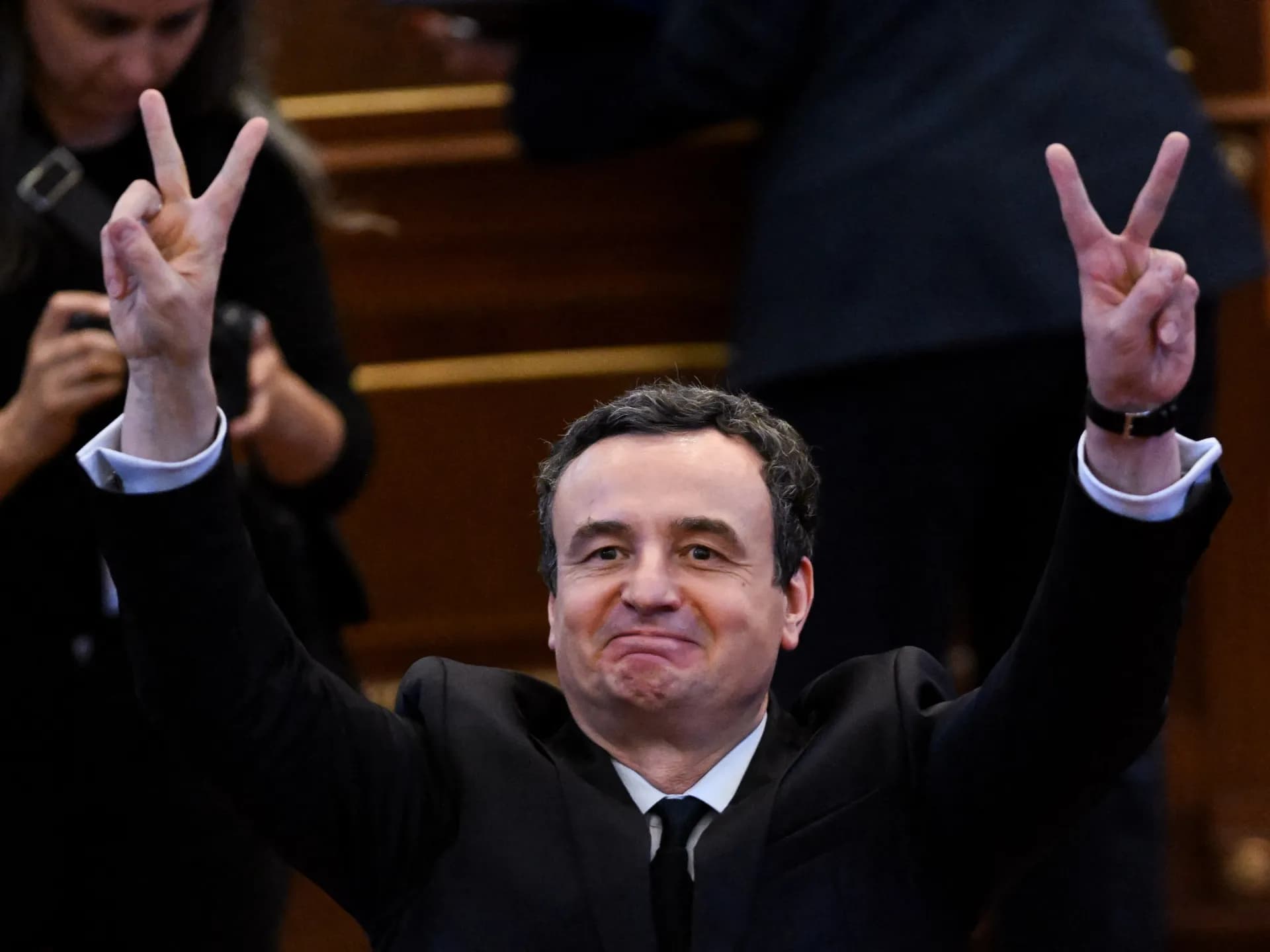 Albin Kurti, de traje oscuro, hace con las dos manos la señal de la victoria en el Parlamento de Kosovo