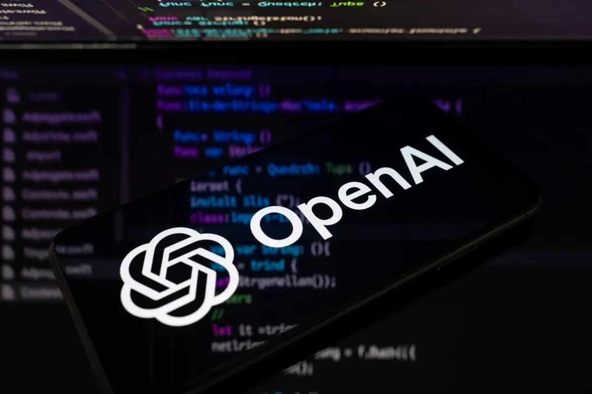 Teléfono celular con el logo de OpenAI frente a una pantalla con código