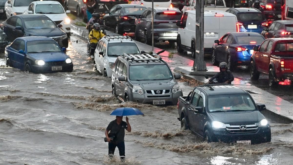 Vehículos y un peatón atraviesan una calle inundada en el norte de Guayaquil