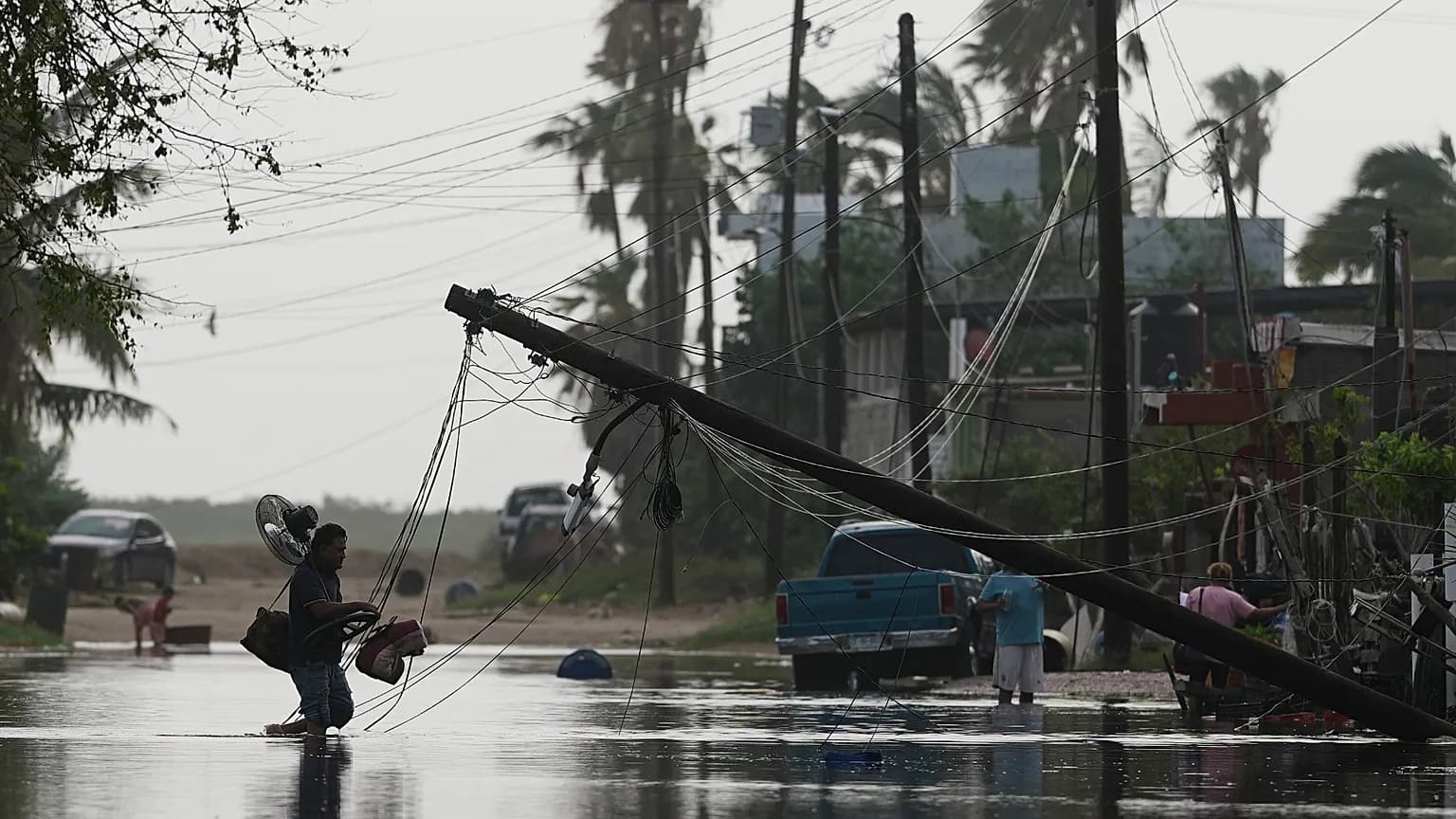 Un hombre carga sus pertenencias por una calle inundada, junto a postes de luz caídos tras el paso del huracán Polo