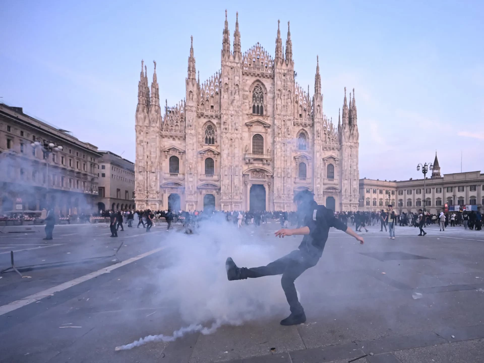 Un manifestante patea una lata de gas lacrimógeno frente a la catedral de Milán