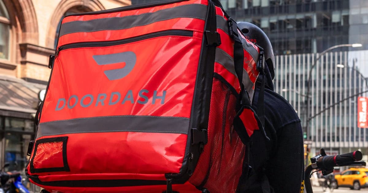 Un repartidor en bicicleta lleva a la espalda una maleta térmica roja de DoorDash por una calle de Nueva York