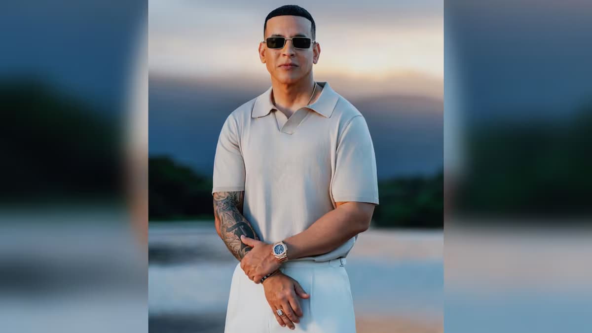 Daddy Yankee posa con gafas oscuras y ropa clara frente a un paisaje al atardecer