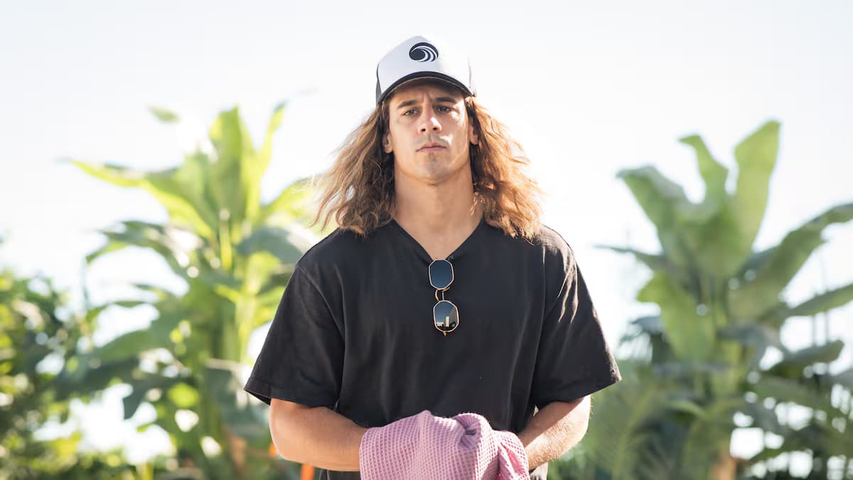 El actor Martiño Rivas, caracterizado como Daniel Sancho, con gorra, camiseta negra y una toalla rosada en las manos