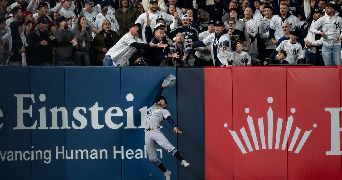 El jardinero de los Rays Víctor Mesa Jr. salta contra la barda mientras aficionados de los Yankees intentan atrapar la pelota