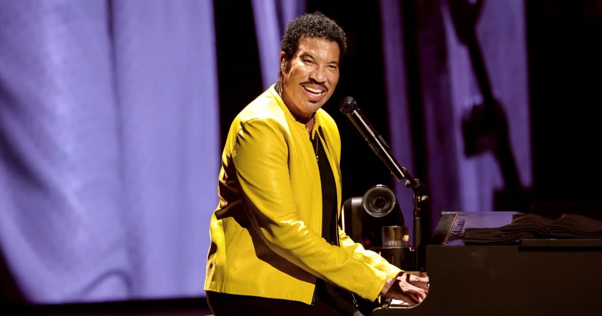 Lionel Richie, con chaqueta amarilla, sonríe mientras toca el piano en un concierto
