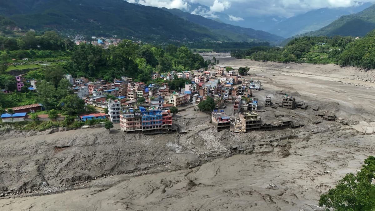 Vista aérea de un poblado nepalí rodeado de lodo y escombros tras el paso de la riada, con edificios destruidos junto al cauce