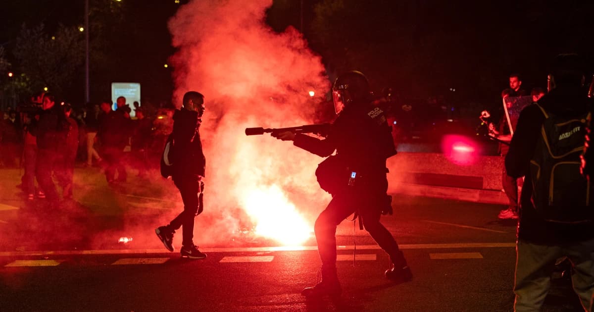Un policía antidisturbios frente a manifestantes y bengalas en Madrid durante la protesta por el accidente ferroviario