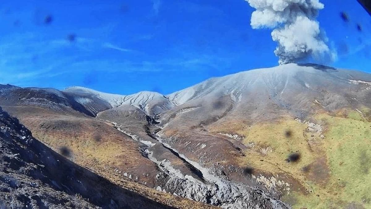 Columna de ceniza saliendo del cráter del volcán Puracé sobre las laderas cubiertas de material gris, bajo un cielo azul