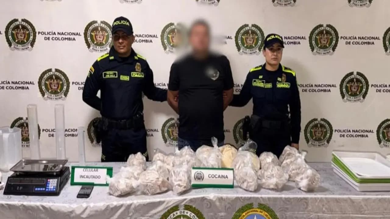 Dos policías custodian al capturado detrás de una mesa con paquetes de cocaína, una báscula y un celular incautados en Medellín