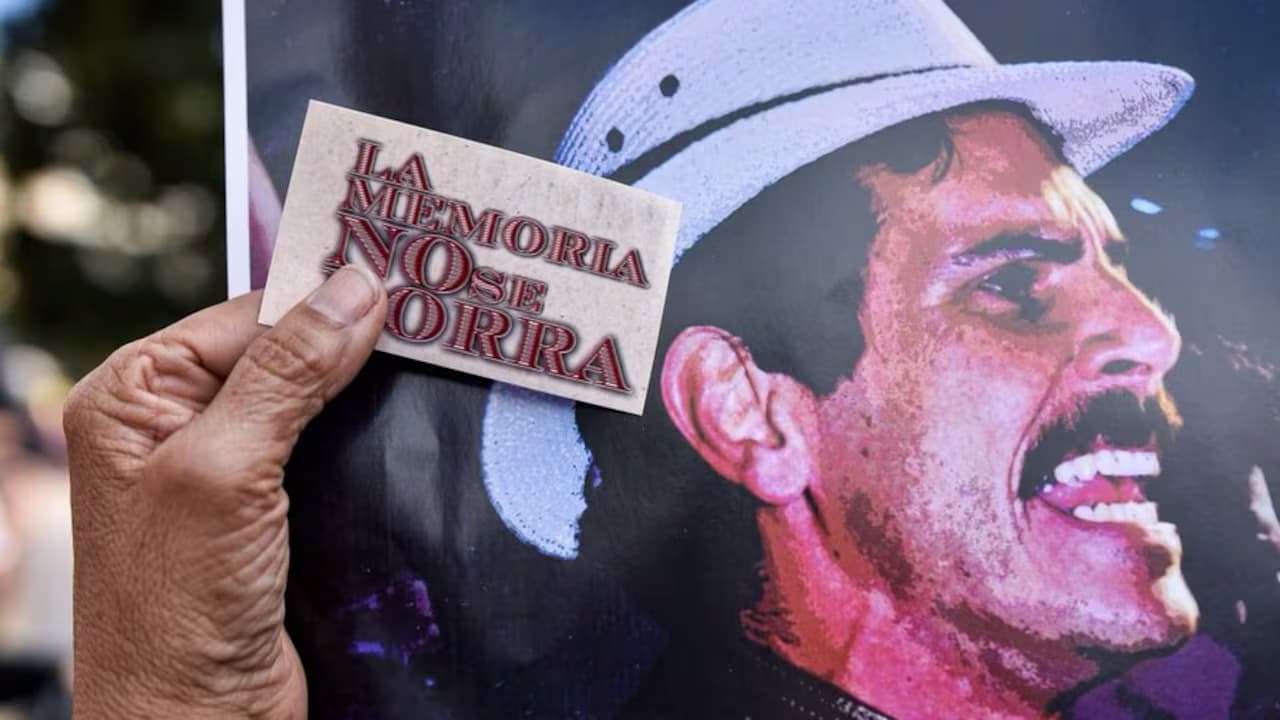 Una mano sostiene un letrero con la frase «La memoria no se borra» sobre un afiche de Carlos Pizarro