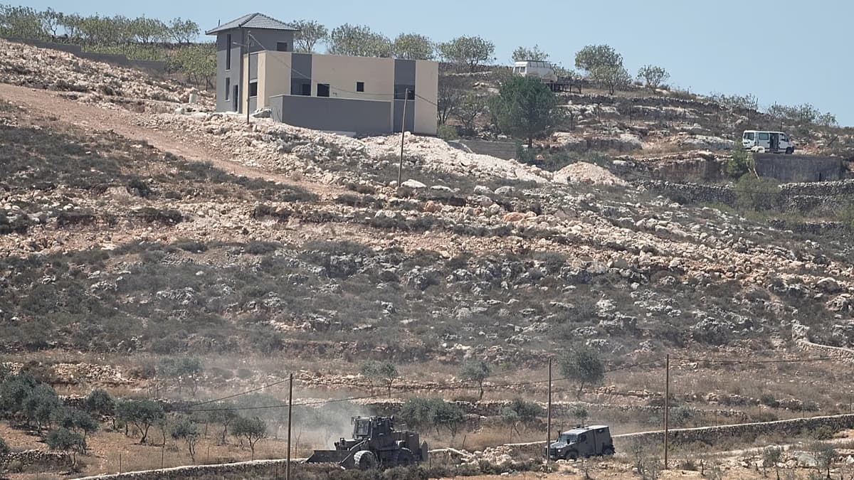 Una excavadora y un vehículo militar trabajan en una ladera pedregosa junto a una construcción de bloques claros