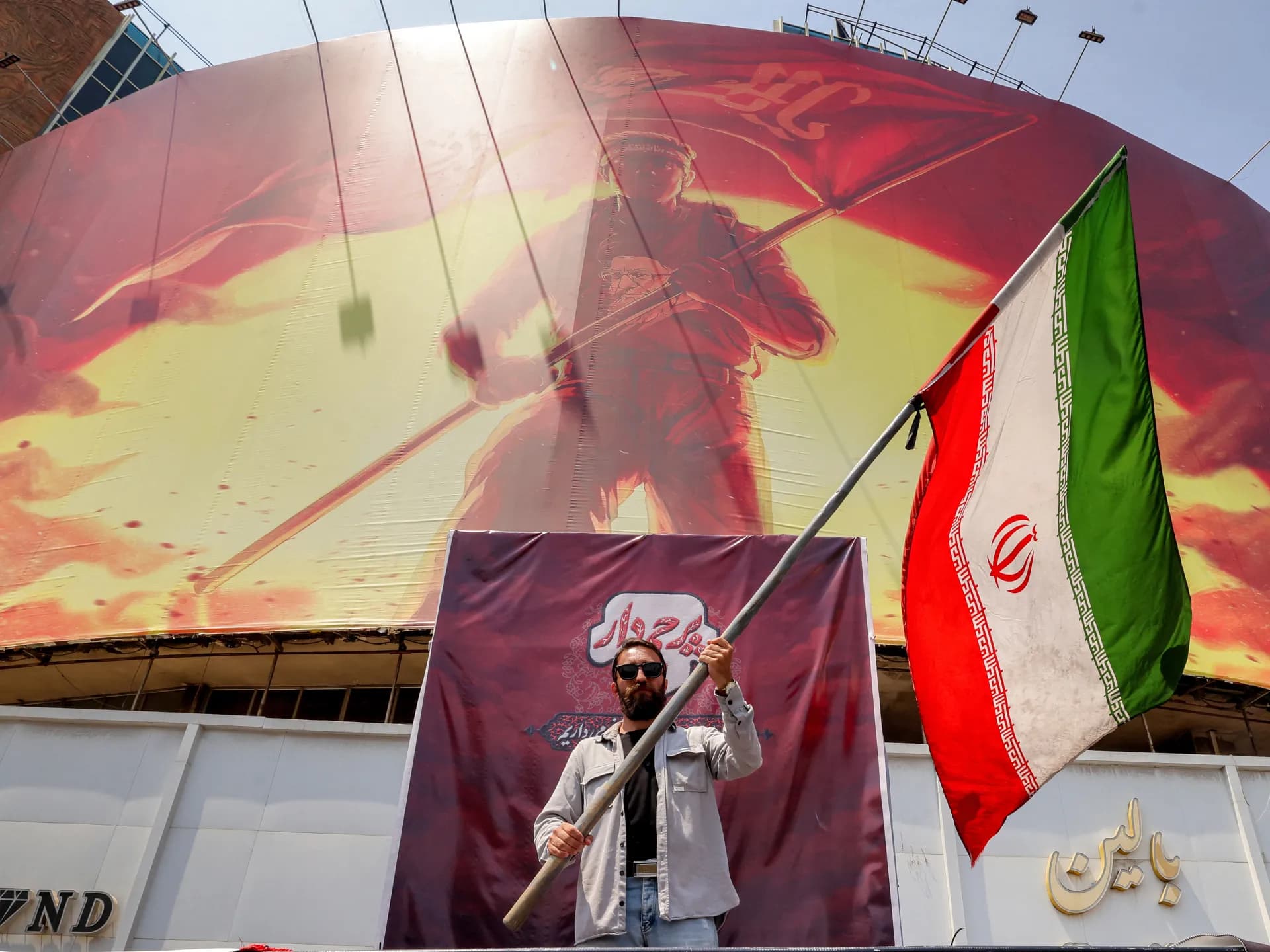 Un hombre ondea una bandera iraní frente a una valla política en la plaza Valiasr, en el centro de Teherán