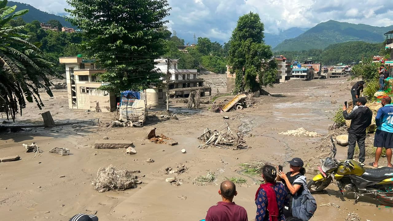 Un pueblo cubierto por lodo y escombros tras la crecida, con casas destruidas y vecinos mirando desde una ladera