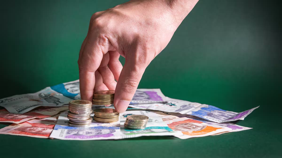 Una mano toma monedas sobre billetes colombianos