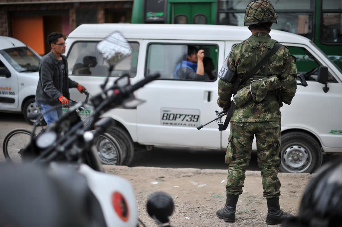 Un soldado del Ejército, de espaldas y con fusil, vigila una calle con vehículos y transeúntes