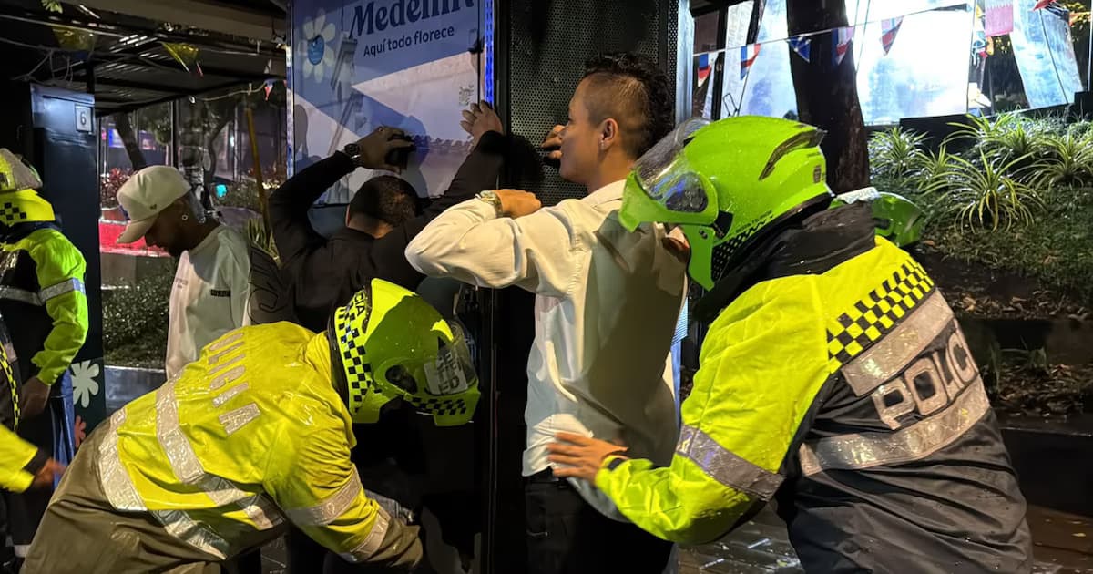 Policías requisan a varios hombres durante un operativo nocturno bajo la lluvia en el Parque Lleras de Medellín