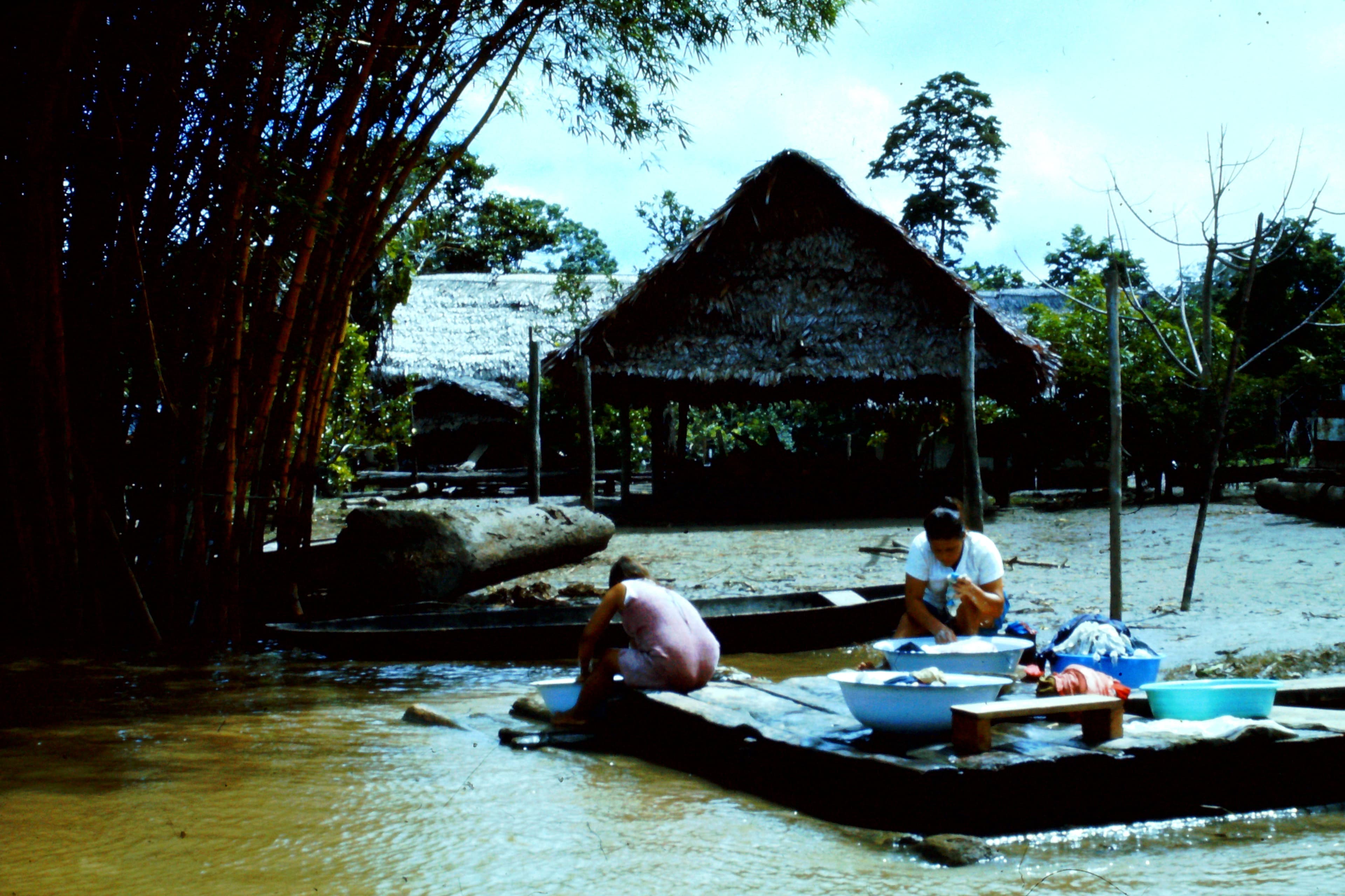 Dos mujeres lavan ropa sobre una balsa a la orilla del río Amazonas, frente a casas con techo de palma, río abajo de Iquitos, en la región de Loreto, en una fotografía de archivo