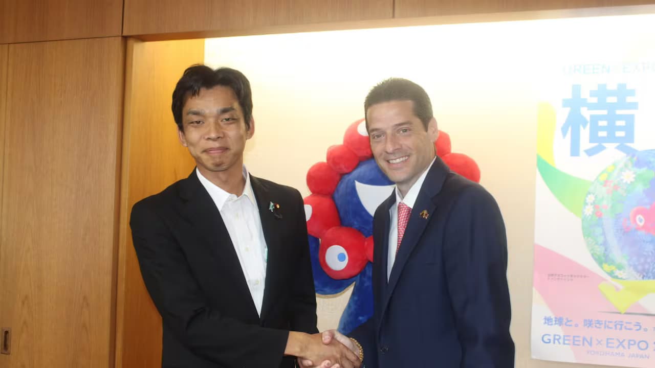 El ministro de Comercio de Colombia estrecha la mano de un funcionario japonés en una oficina en Tokio