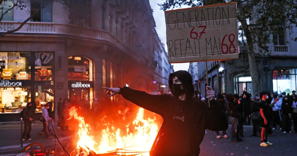 Un manifestante encapuchado con un cartel señala junto a una barricada en llamas en una calle de París