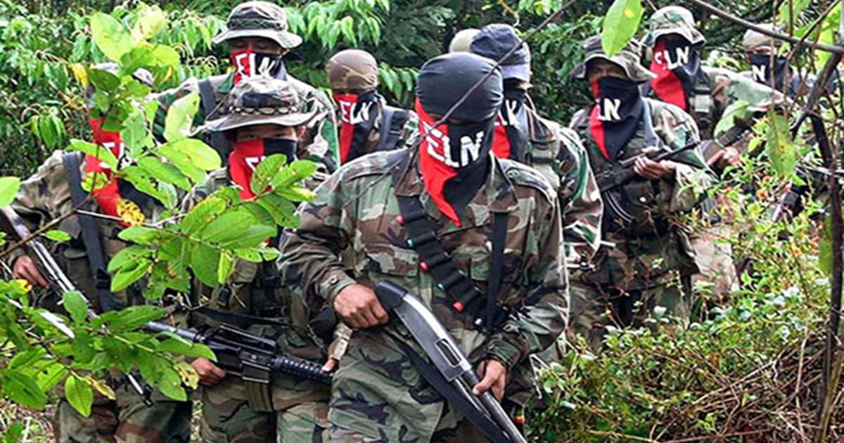 Guerrilleros del ELN con armas y pañoletas caminan en fila por una zona selvática