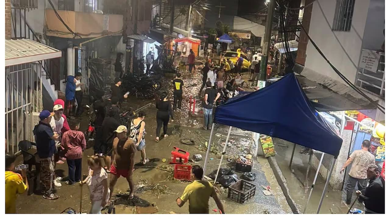 Vecinos en una calle cubierta de lodo y escombros tras la creciente de la quebrada La Iguaná, en Medellín