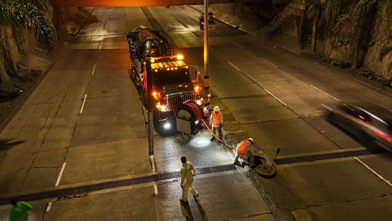 Operarios con un camión de succión limpian un sumidero en un soterrado vial de Medellín durante la noche