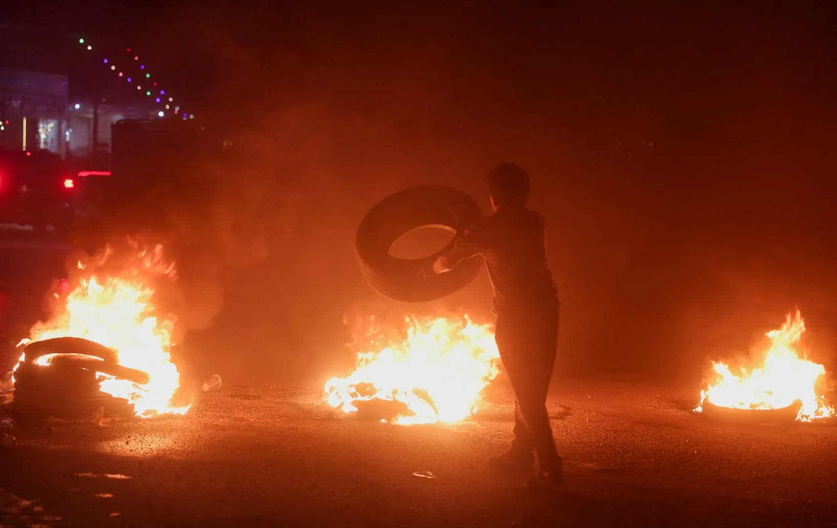 Un manifestante arrastra un neumático entre fogatas encendidas en una calle de Siria durante la noche