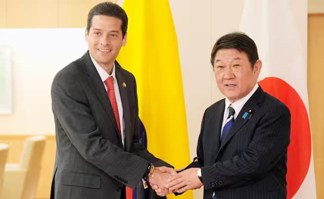 Dos hombres de traje se estrechan la mano ante las banderas de Colombia y Japón en un salón oficial