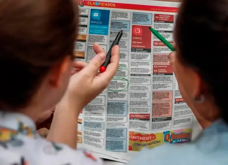 Dos personas de espaldas revisan con marcadores la sección de clasificados de empleo de un periódico