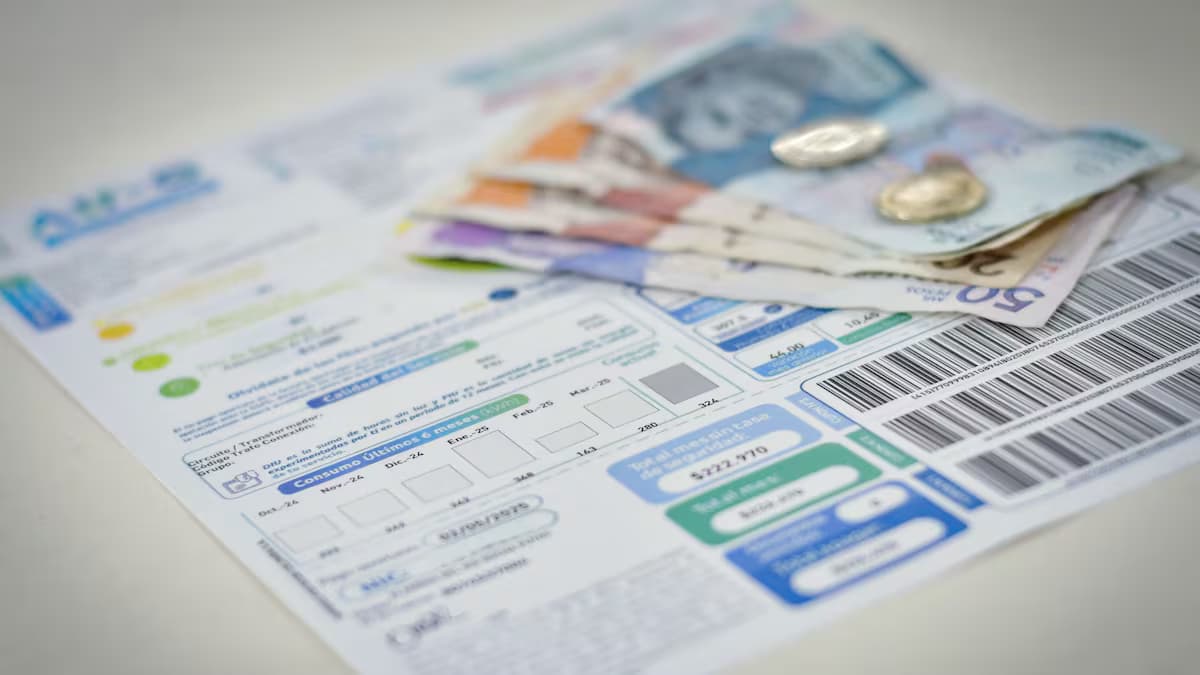 Una factura de energía eléctrica sobre una mesa junto a billetes y monedas colombianas
