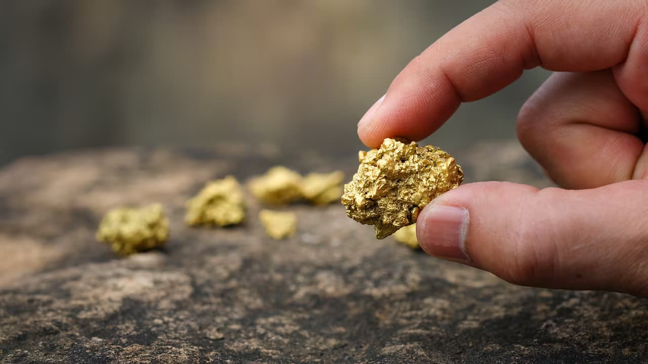 Mano que sostiene una pepita de oro sobre una roca