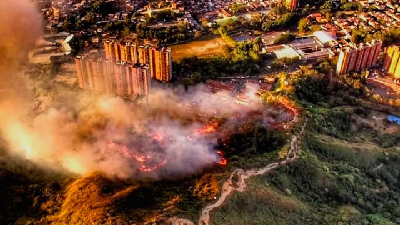 Vista aérea de un incendio de cobertura vegetal en una ladera de Medellín, con humo sobre los edificios del barrio contiguo