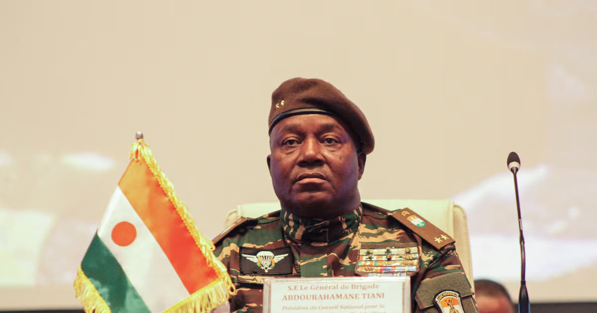 El general Abdourahamane Tiani, con boina y uniforme de camuflaje, sentado en una mesa junto a una bandera de Níger y un micrófono, durante un acto oficial