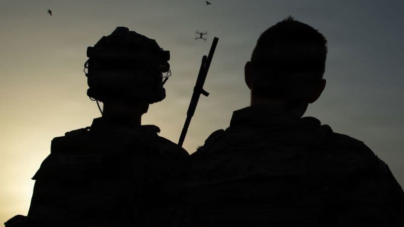 Siluetas de dos militares al atardecer con un dron en el cielo