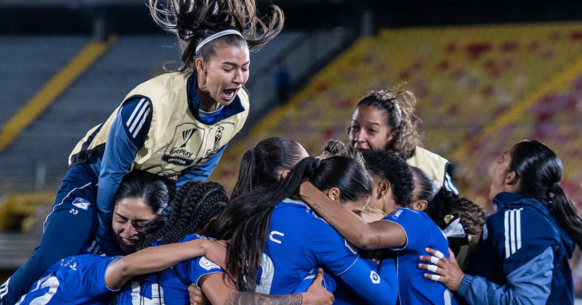 Jugadoras de Millonarios se abrazan para celebrar en un estadio