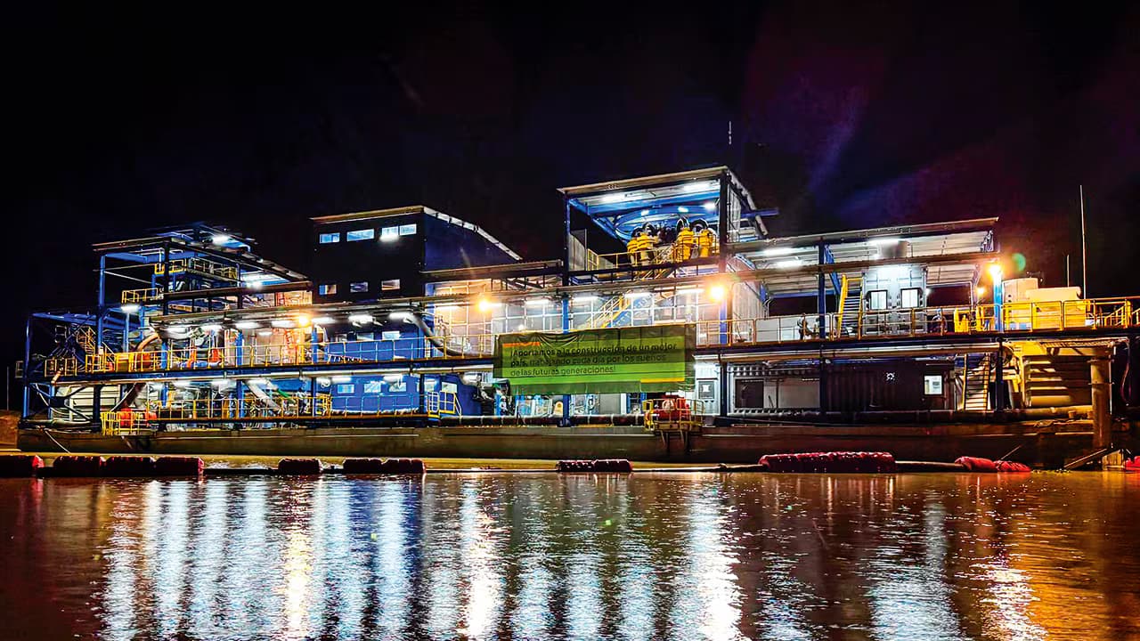 Draga de explotación aurífera de Mineros iluminada de noche sobre el río