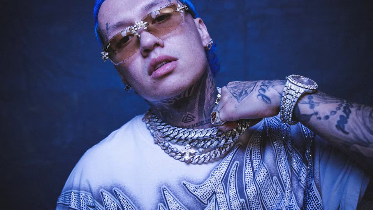 Retrato del cantante Blessd con gafas, cabello azul y cadenas plateadas