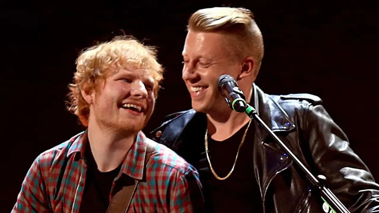 Ed Sheeran y Macklemore sonríen juntos frente a un micrófono en un escenario