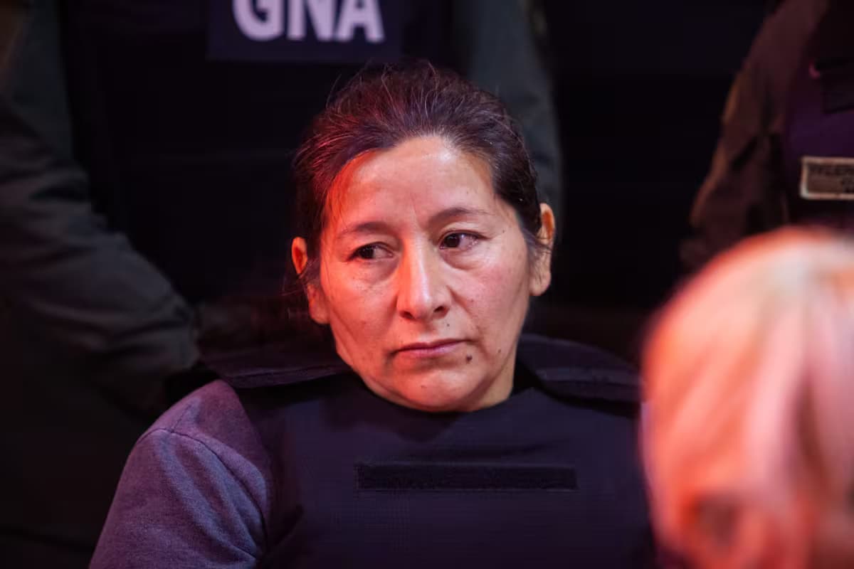 Una mujer con chaleco antibalas sentada en una sala, rodeada de agentes de la Gendarmería argentina