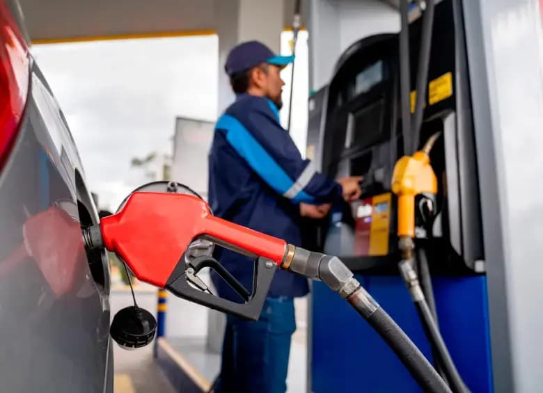 Una manguera de gasolina en el tanque de un vehículo mientras un empleado opera el surtidor en una estación de servicio
