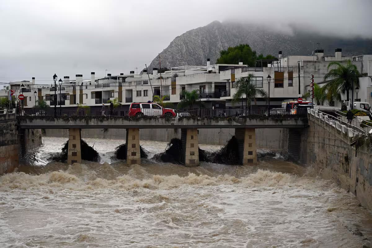Un río crecido pasa bajo un puente mientras un vehículo de bomberos lo cruza en el este de España