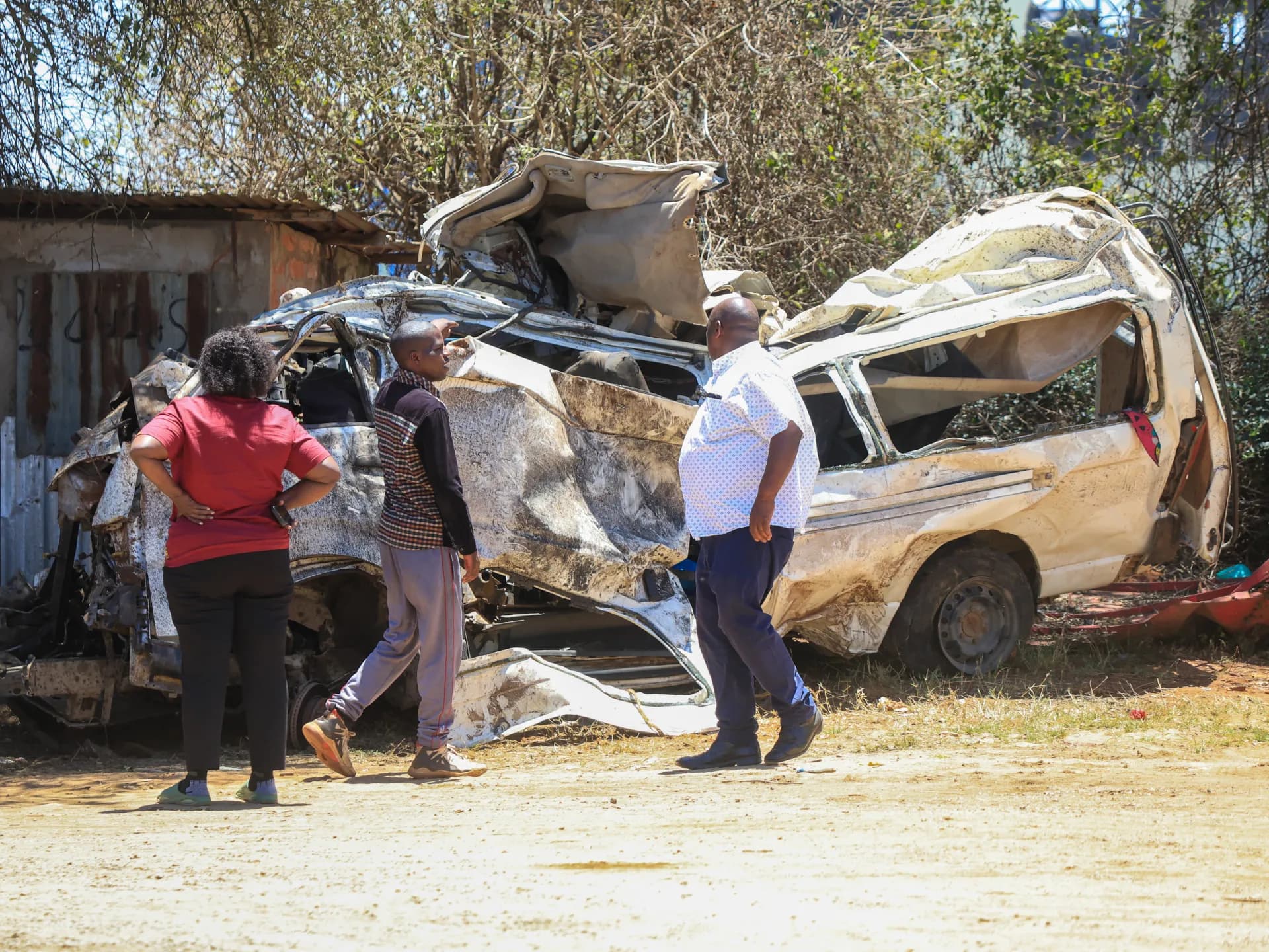 Tres personas observan los restos destrozados del minibús que transportaba a los peregrinos en Kenia