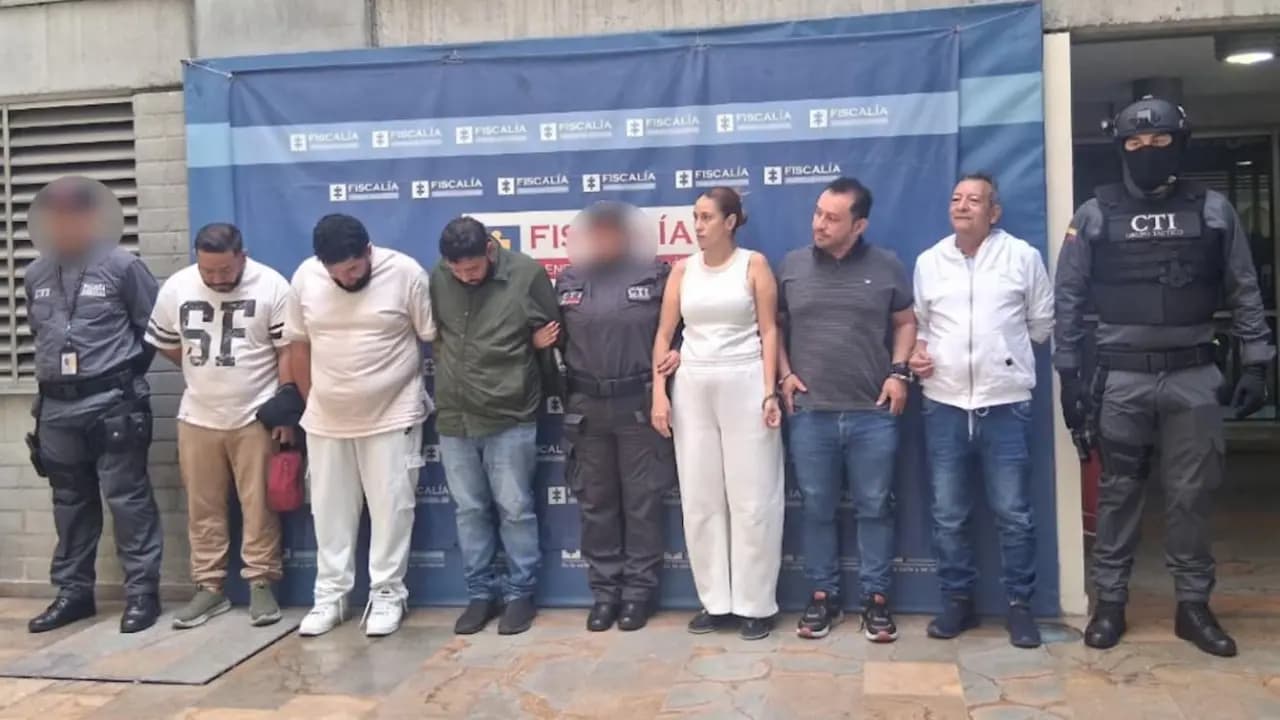 Los seis procesados, custodiados por agentes del CTI, frente a un pendón de la Fiscalía en Medellín