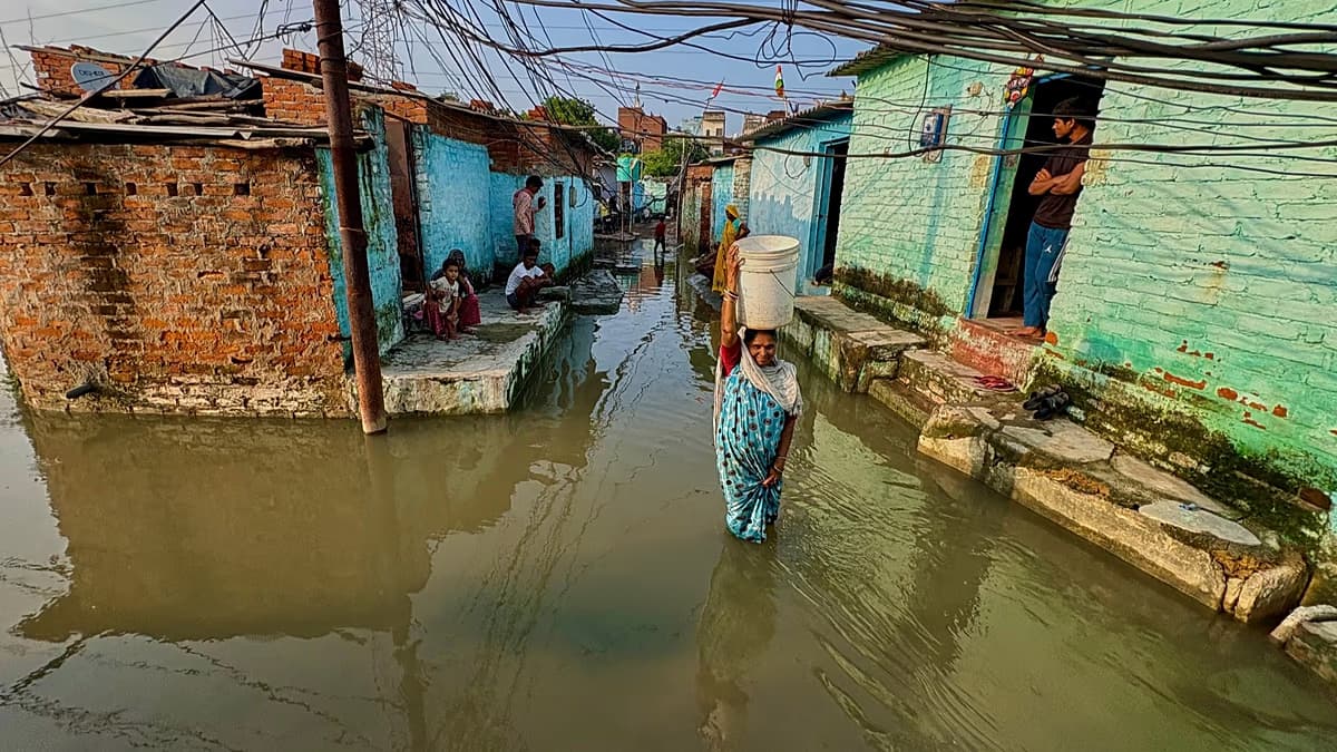 Una mujer camina con un balde en la cabeza por una calle inundada entre casas de ladrillo en el norte de la India