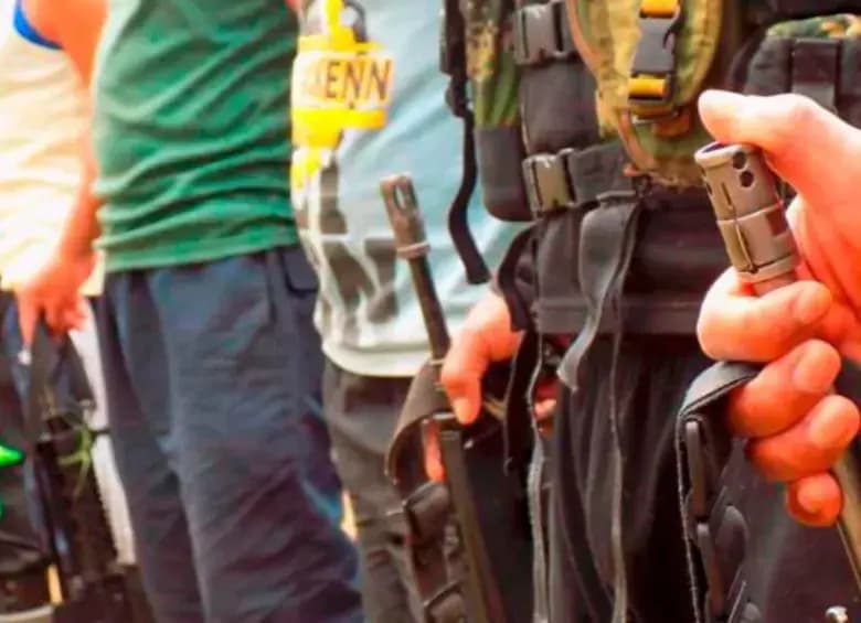 Hombres armados con fusiles y equipo de campaña de pie junto a jóvenes vestidos de civil en una zona rural