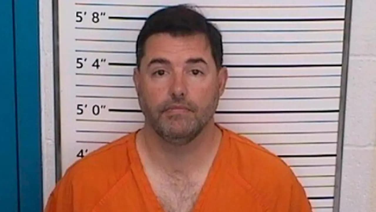 Fotografía de reseña policial de Jed York, con uniforme naranja de detenido, frente a la escala de estatura de una comisaría