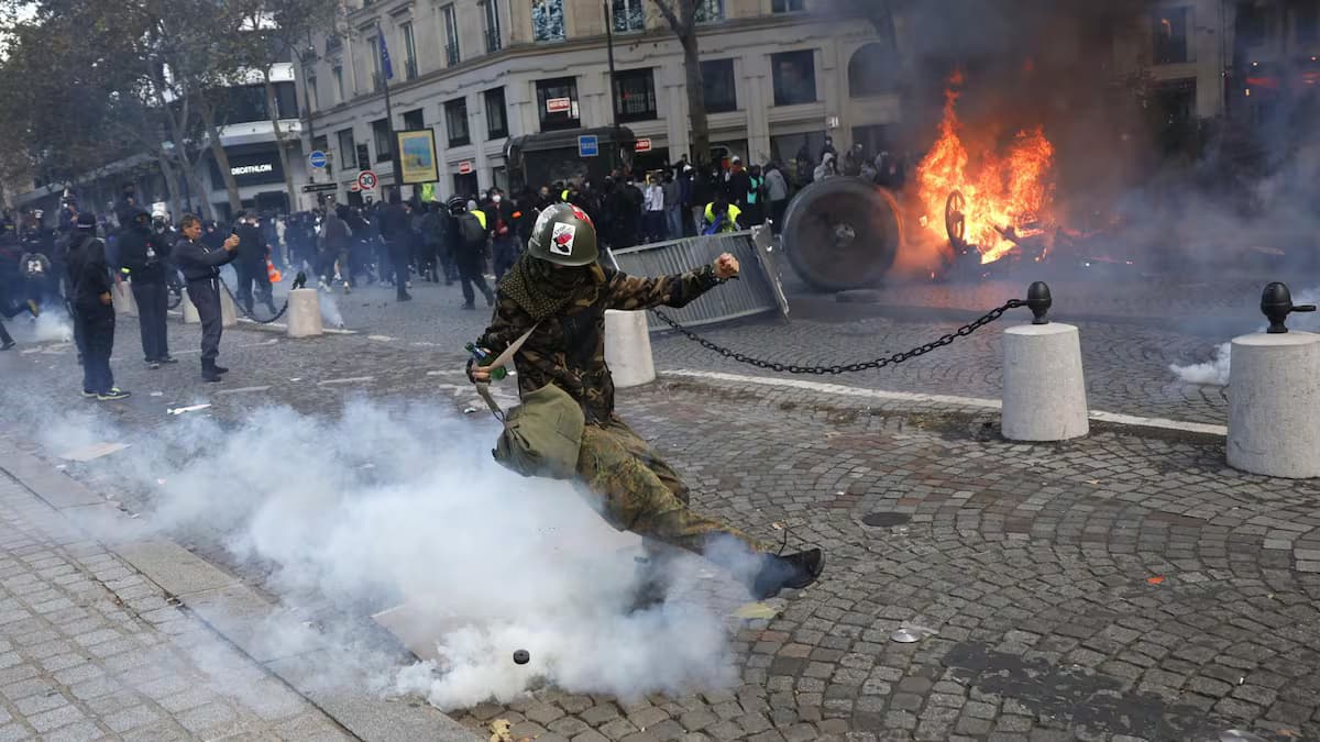 Un manifestante con casco patea una granada de gas lacrimógeno junto a una barricada en llamas en París