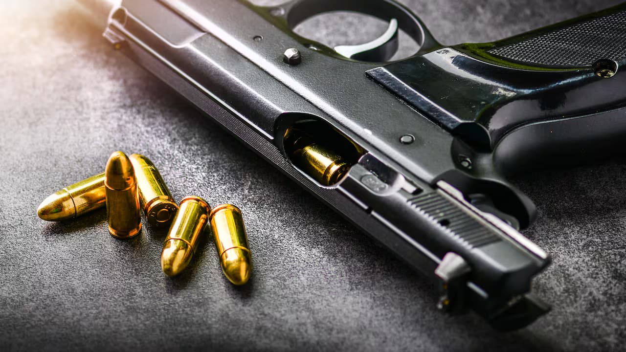Una pistola y varios cartuchos sobre una superficie oscura